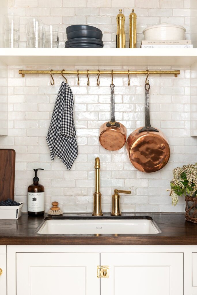 White brick tiled backsplash with hanging pots above sink
