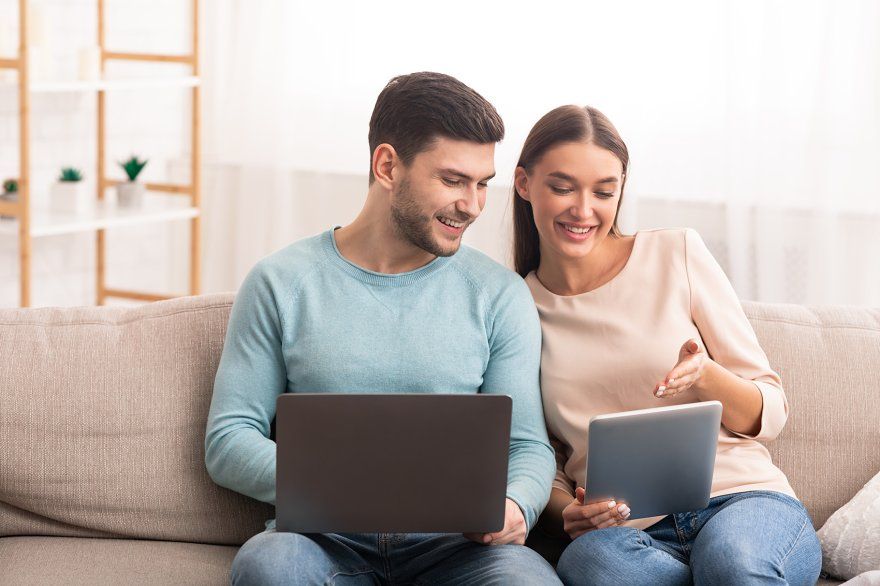 Couple smiling on couch looking at laptop and tablet