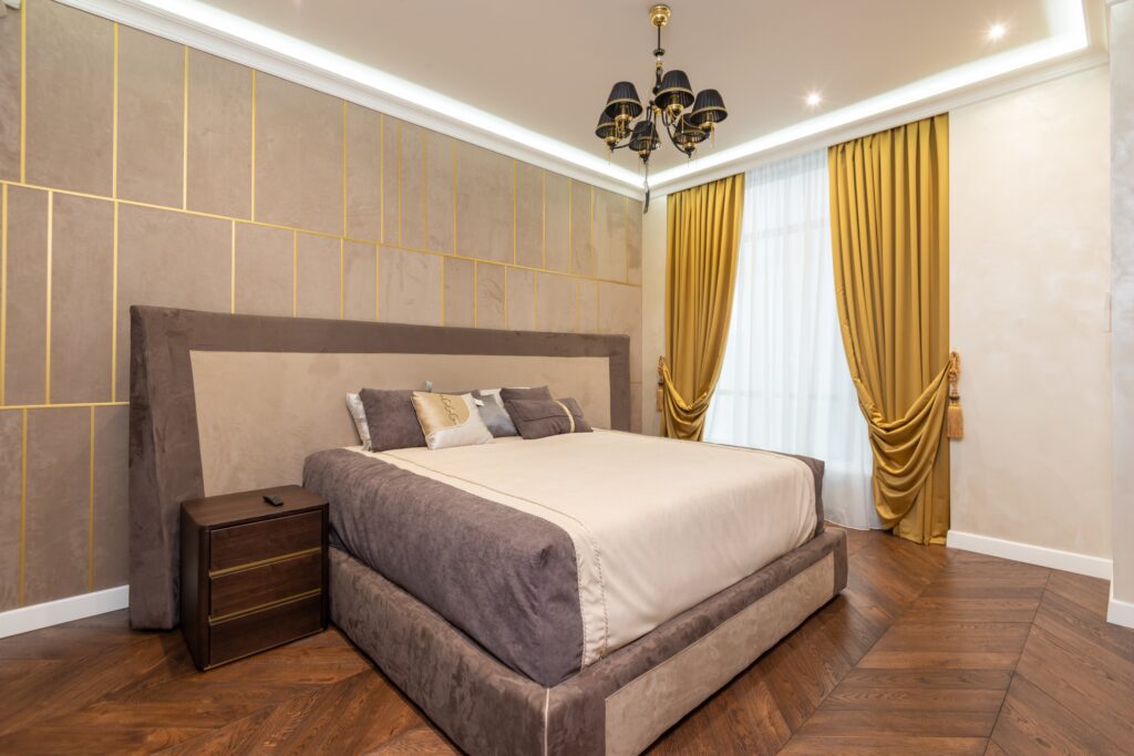 Accented bedroom with golden curtains and a cut-out tile-styled backboard wall behind a king-sized bed