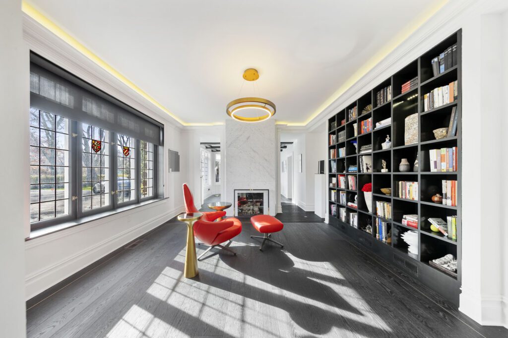 Black living room with bookcase, red luxury lounge chairs, and open windows