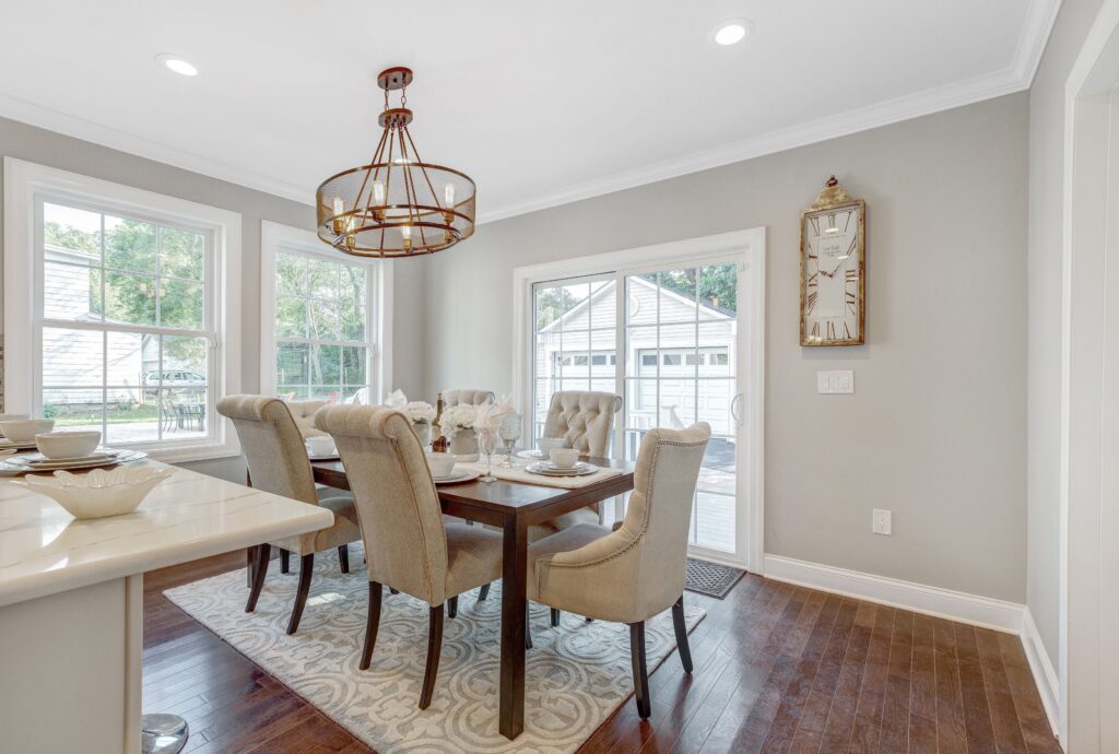 Elegant dining area with six upholstered chairs around a wooden table, surrounded by large windows and a sliding door, featuring a modern chandelier and neutral decor.