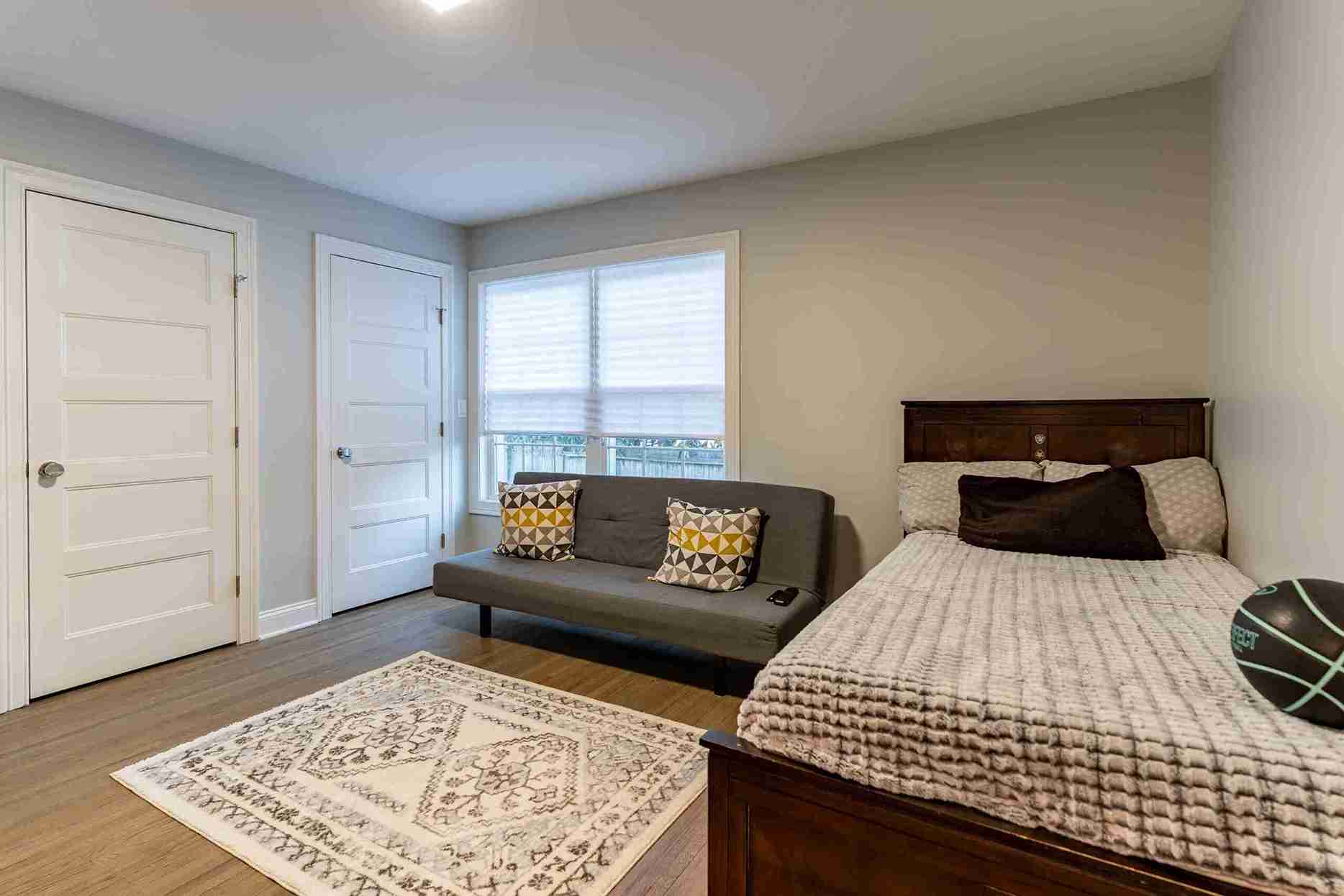 Cozy bedroom with warm wood floors, single bed, modern gray futon, geometric pillows, neutral walls, and soft lighting for a calm, inviting atmosphere.