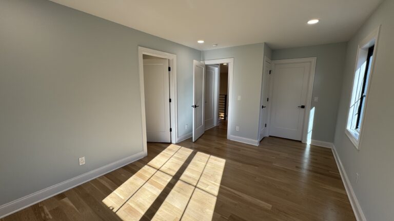 How Much Does It Cost to Extend a Room. Bright, finished room with vaulted ceiling, modern pendant lighting, light wood flooring, and multiple white doors.
