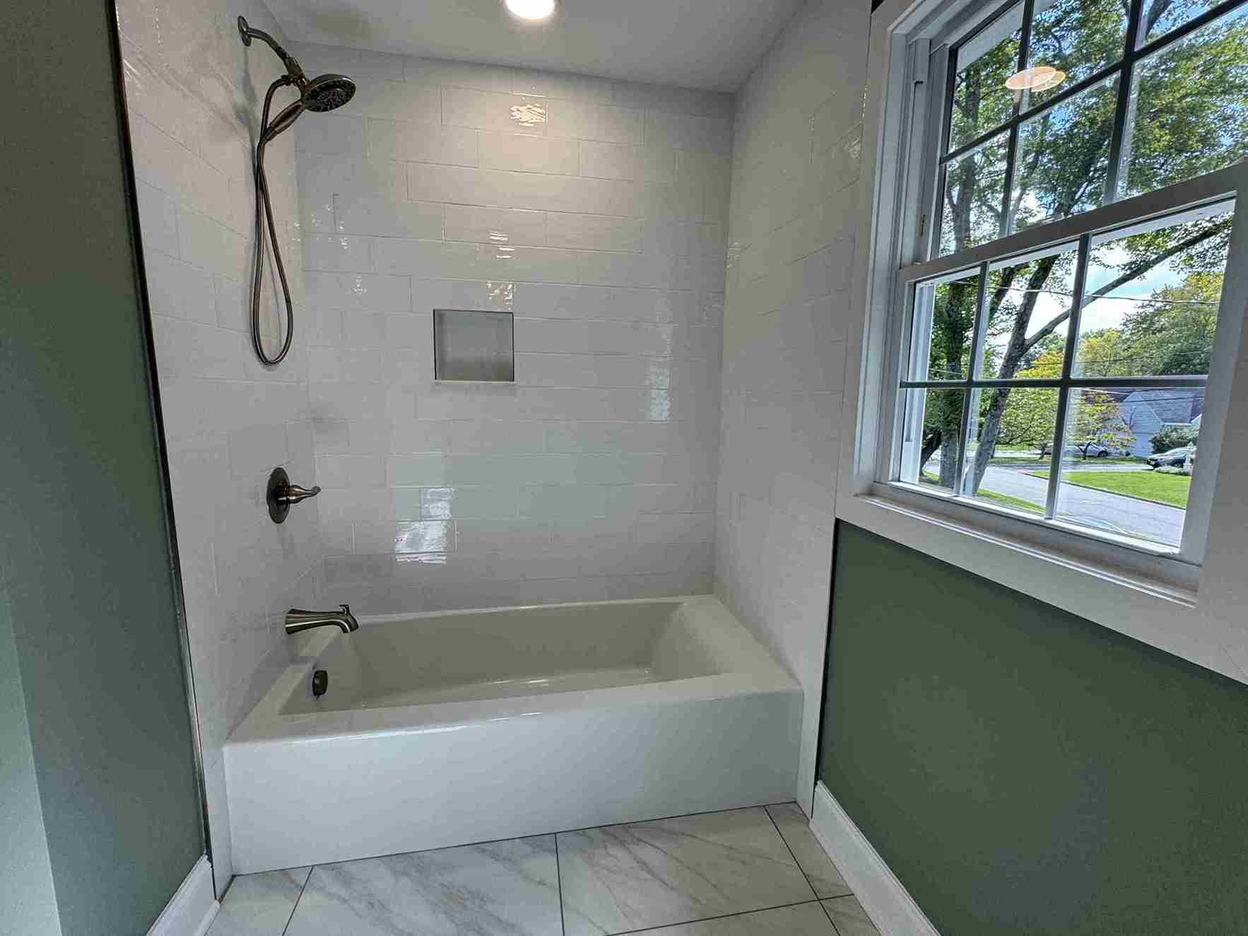 Spacious bathroom renovation in Bergenfield home featuring freestanding tub, floor-to-ceiling tile, skylight and floating vanities.