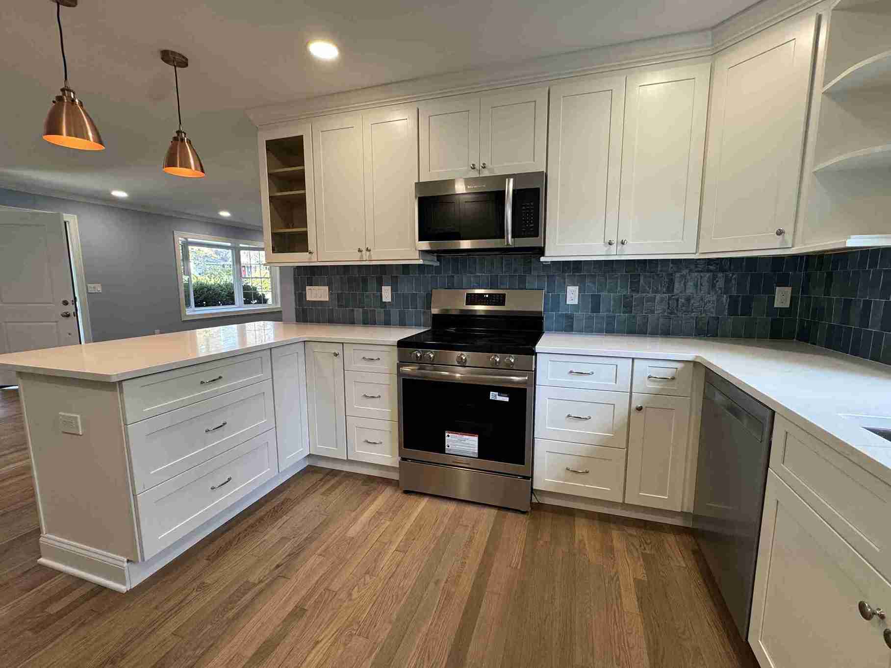 Bright minimalist kitchen redesign with white cabinetry, waterfall island, brass hardware, integrated appliances and pendant lighting