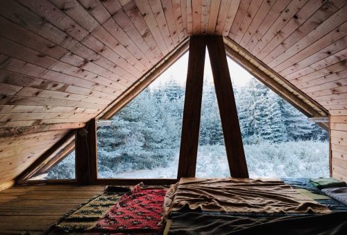 A cozy attic bedroom facing a window showing a snowy winter's day