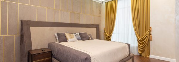 Accented bedroom with golden curtains and a cut-out tile-styled backboard wall behind a king-sized bed