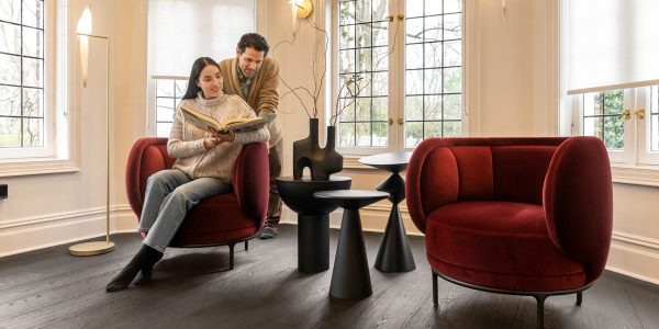 Woman reading in a plush arm chair with man looking over her shoulder